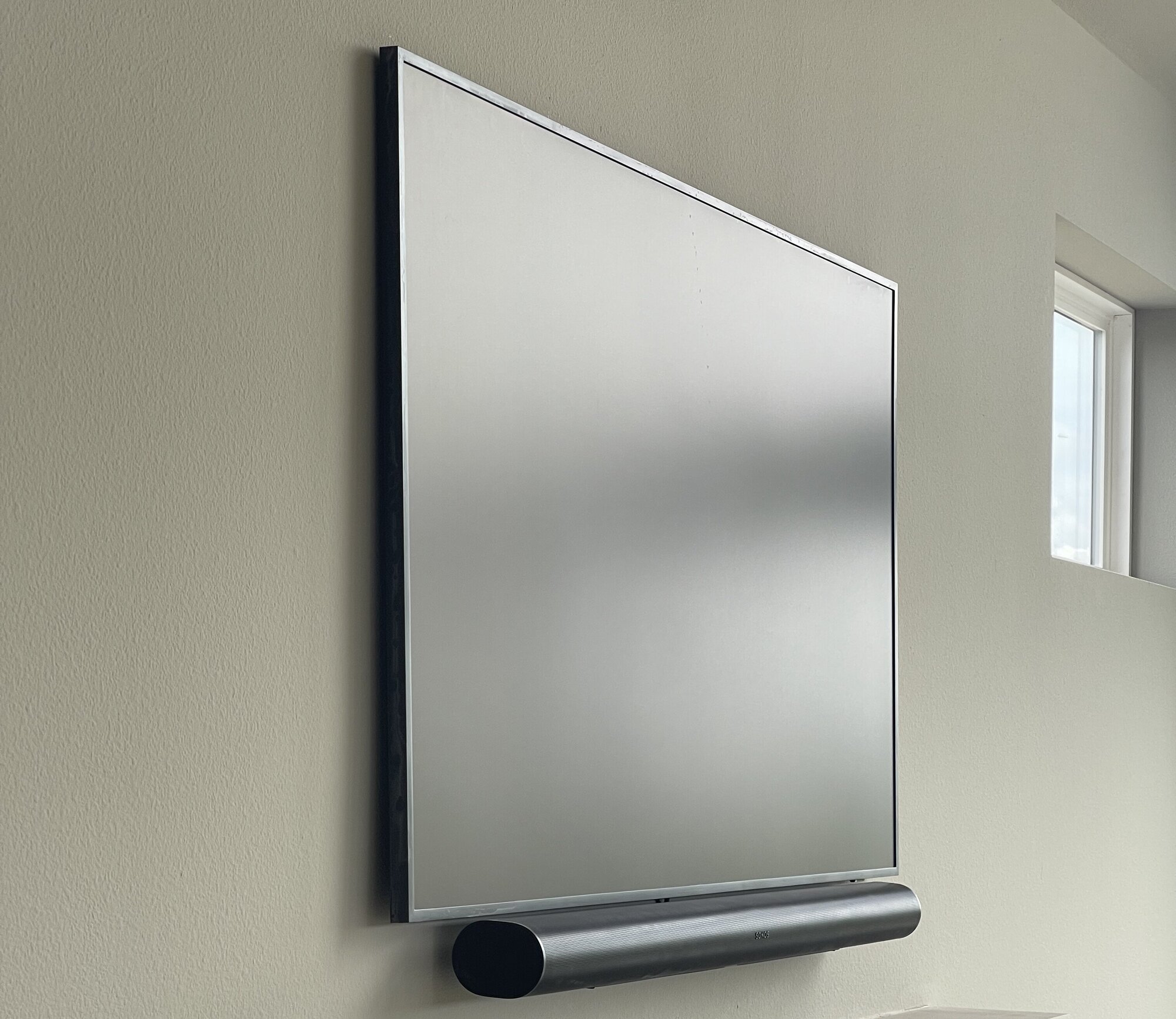 Mirrored television and integrated soundbar mounted above a stone fireplace