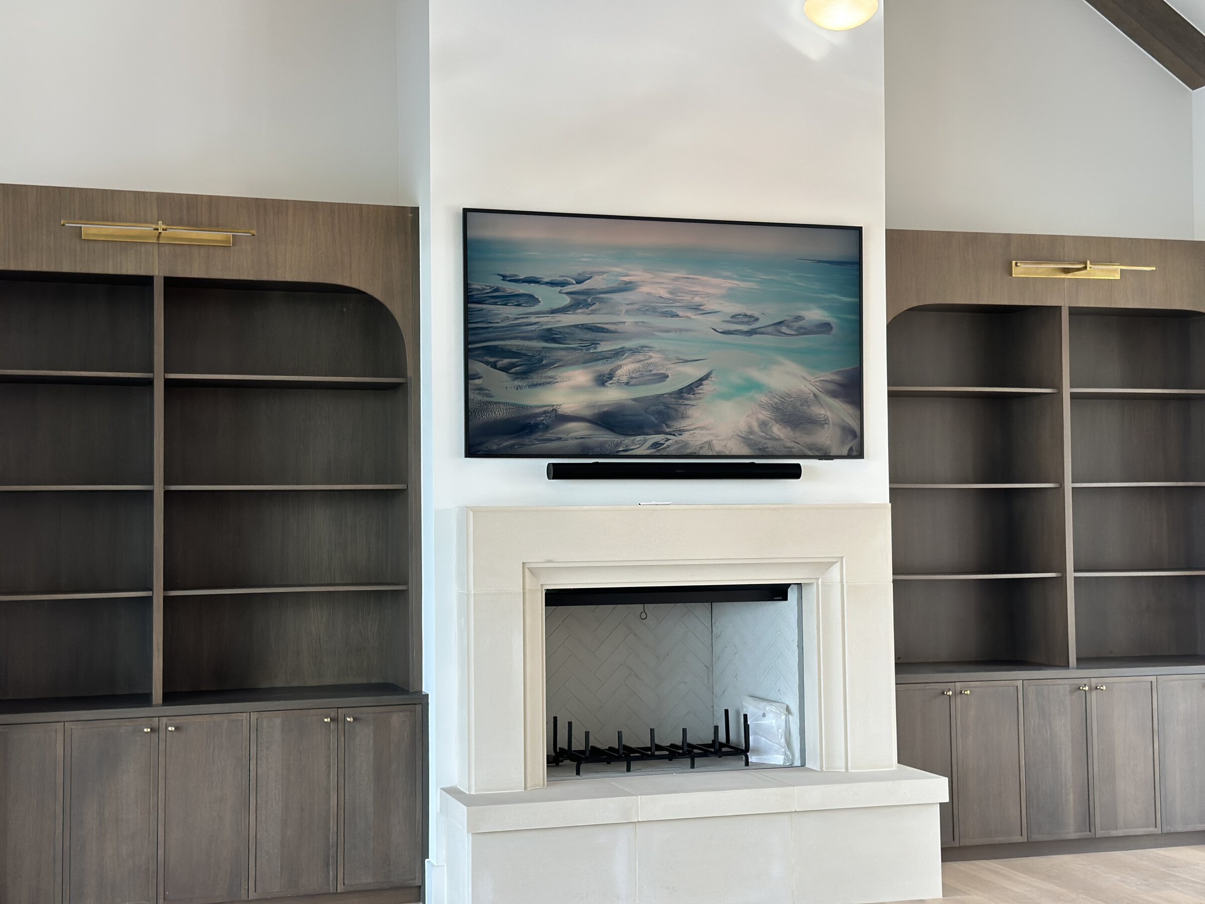 Integrated television above a fireplace flanked by built-in shelving with picture lights