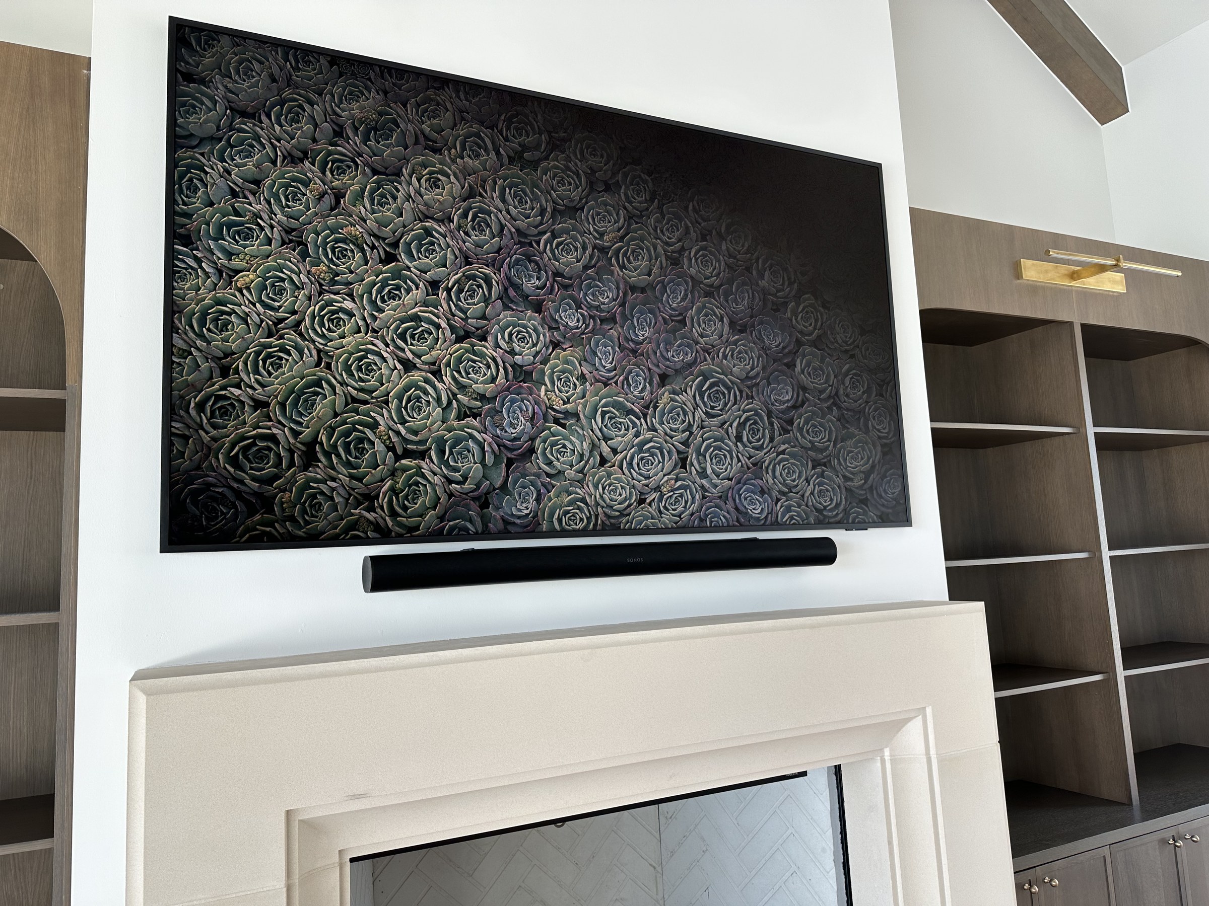 Frame TV and soundbar integrated above a fireplace, flanked by custom built-in shelving
