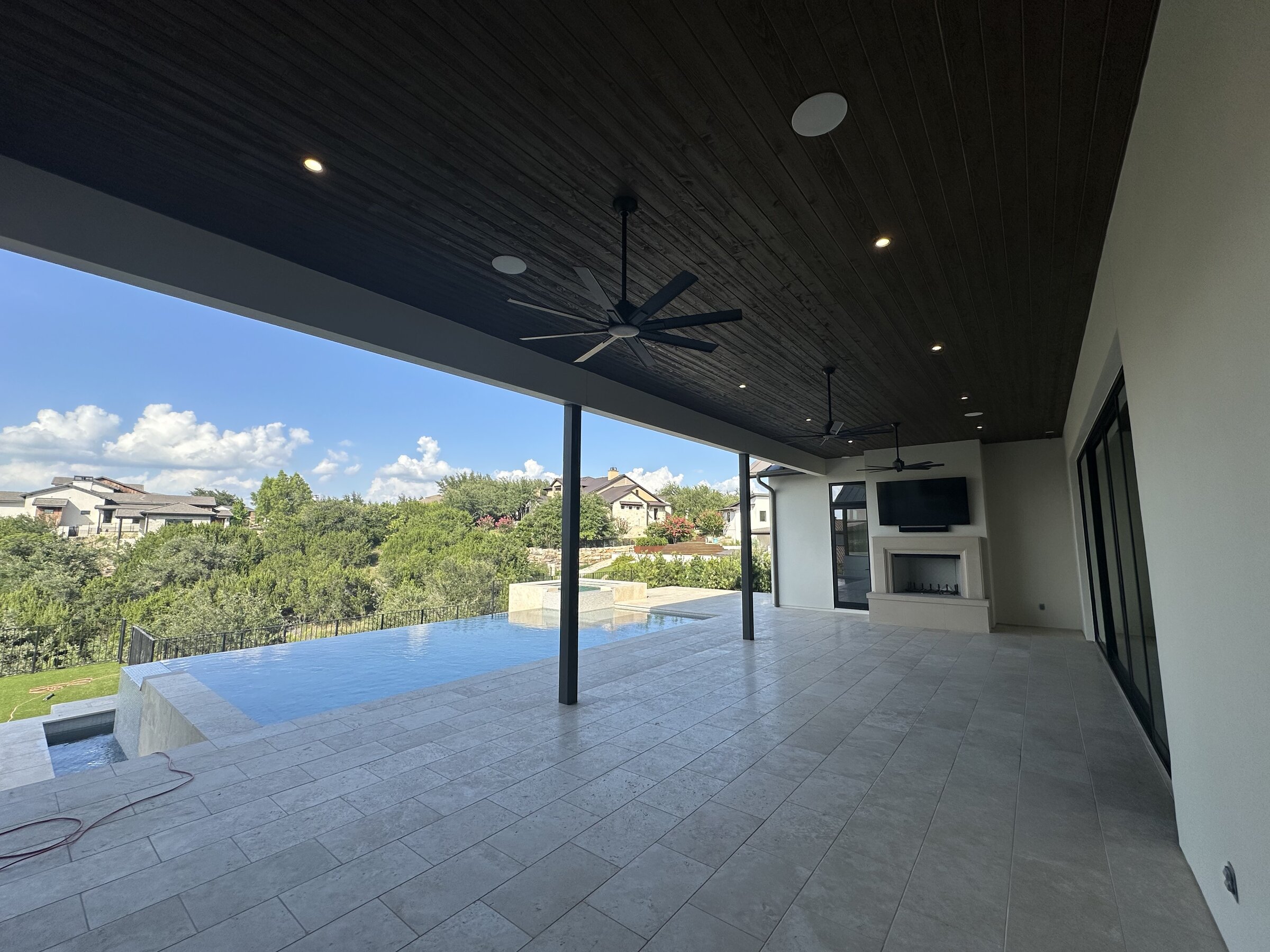 Covered outdoor patio overlooking an infinity pool, with integrated outdoor TV, lighting, and ceiling fans