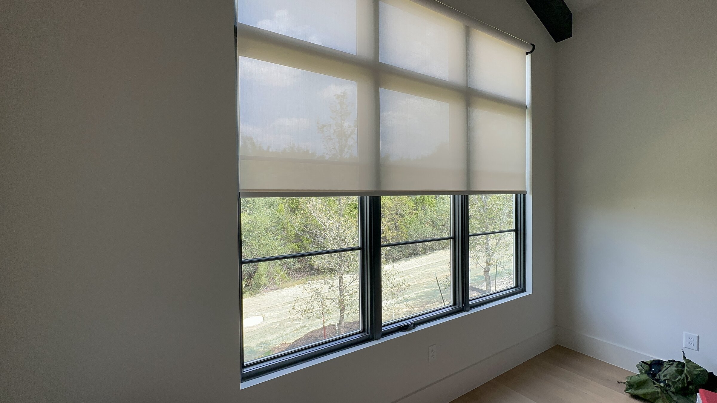 Motorized roller shades on a wall of windows overlooking trees