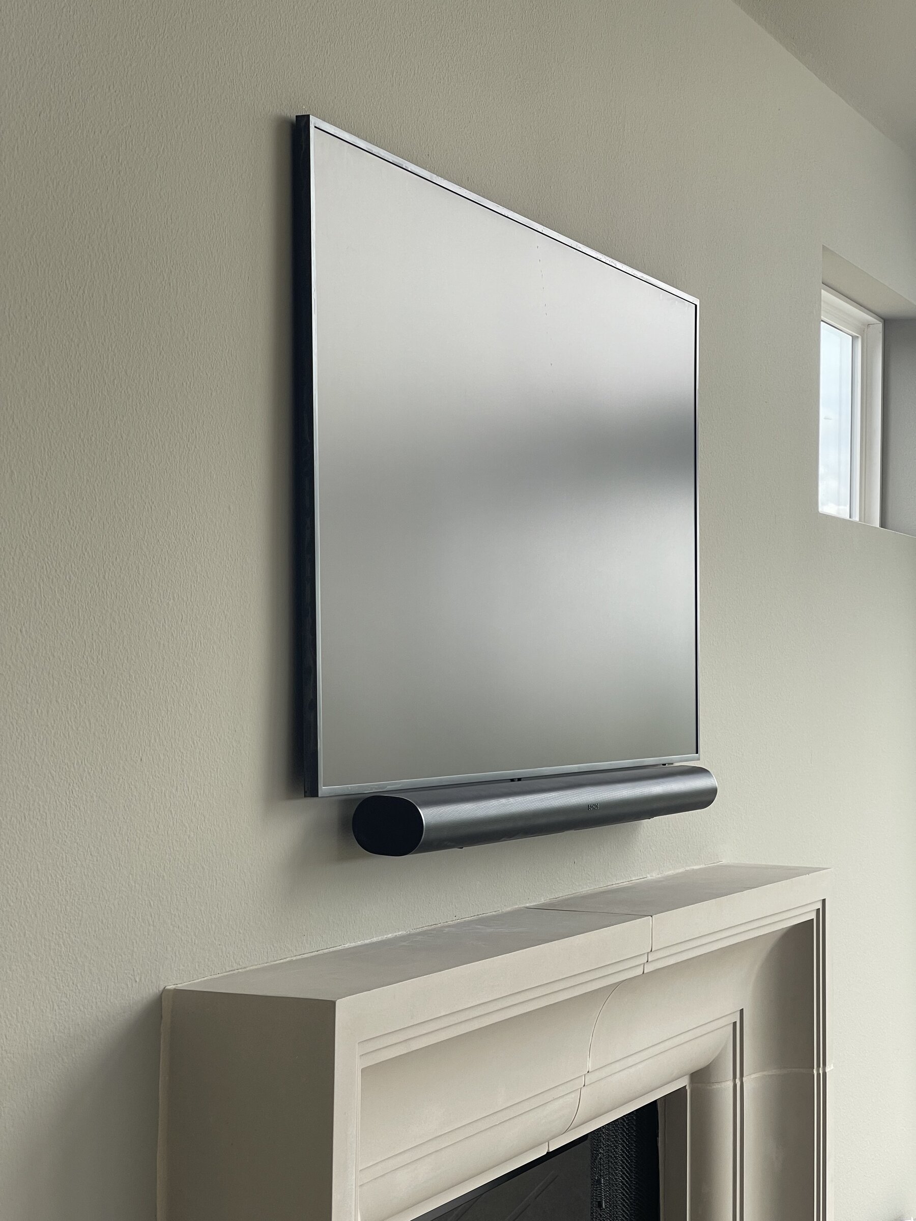 Mirrored television and soundbar integrated above a fireplace