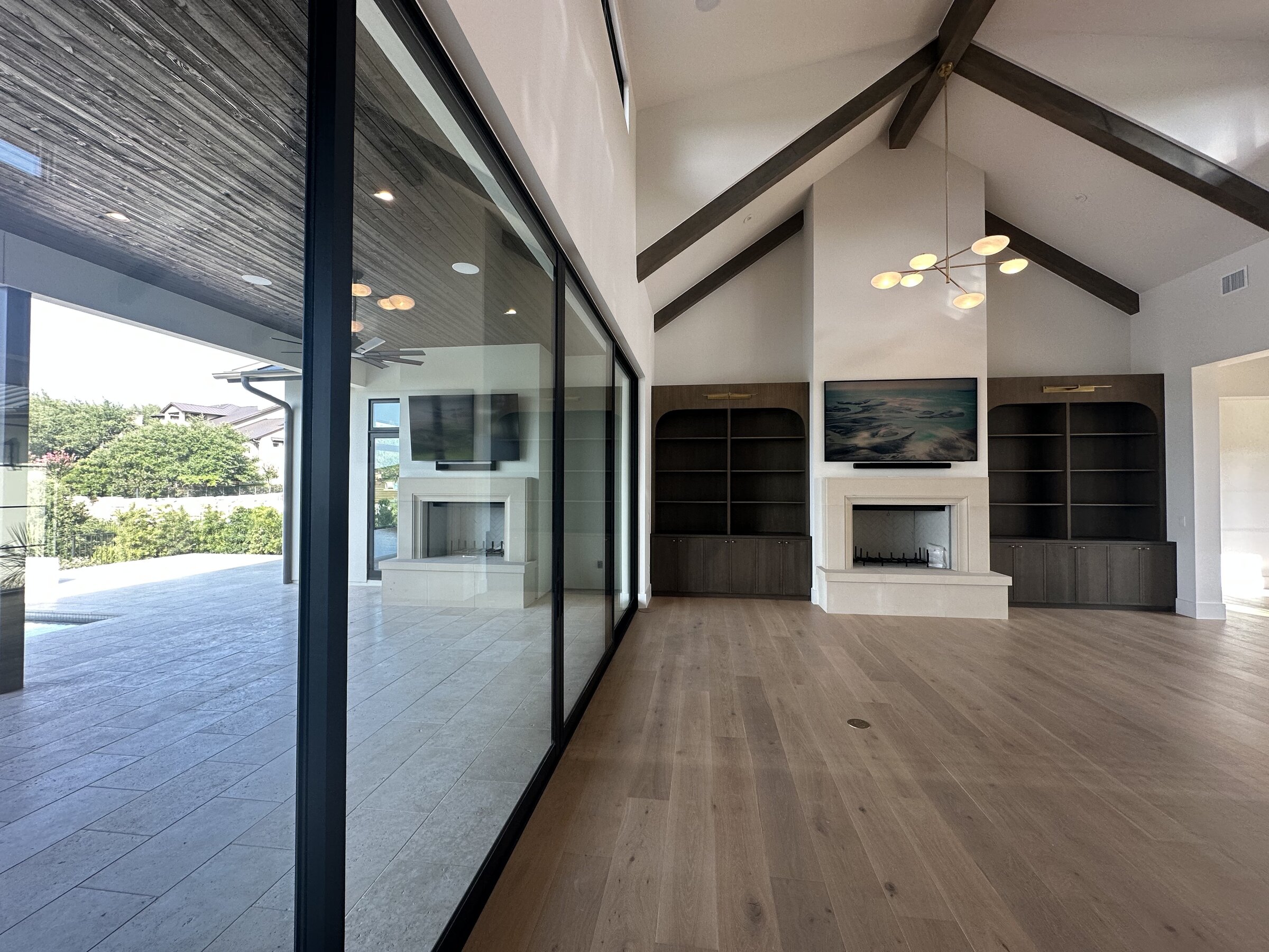 Great room with vaulted wood-beam ceiling, integrated television, fireplace, and glass doors to an outdoor patio